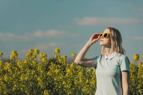 Frau, die ihre Sonnenbrille im Rapsfeld zurechtrückt - VSNF00800