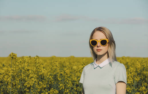 Frau mit blondem Haar und Sonnenbrille im Rapsfeld - VSNF00808