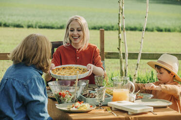 Glückliche Familie beim gesunden Mittagessen am Esstisch im Hinterhof - VSNF00809