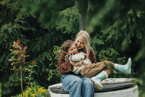 Mutter mit Sohn sitzen zusammen auf einem Brunnen im Garten - VSNF00814