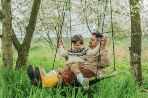 Vater schaukelt mit Sohn im Garten - VSNF00816