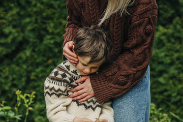 Mutter im braunen Pullover umarmt Sohn im Garten - VSNF00818