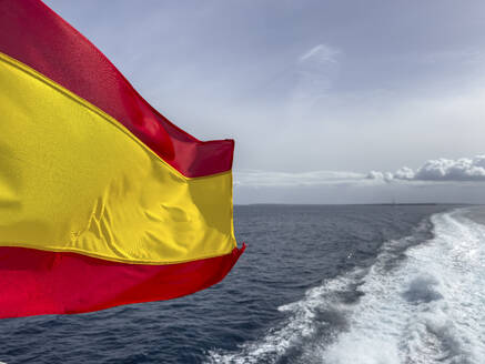 Spanien, Balearische Inseln, Formentera, Wake left by moving boat with Spanish flag fluttering in foreground - MMAF01489