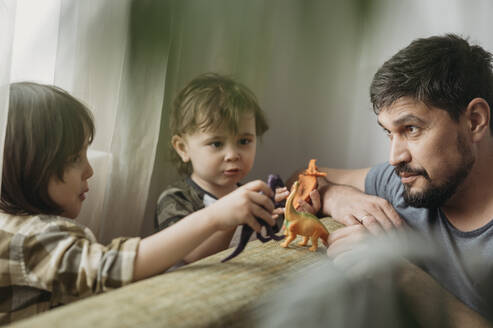 Söhne spielen mit Spielzeugdinosauriern bei ihrem Vater zu Hause - ANAF01404