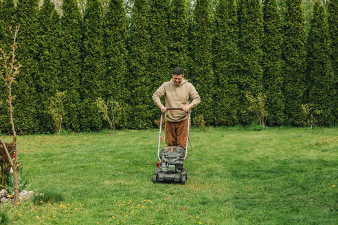 Mann bei der Gartenarbeit mit Rasenmäher im Hinterhof - VSNF00819