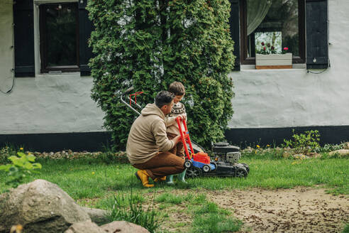 Father assisting son with lawnmower in back yard - VSNF00823