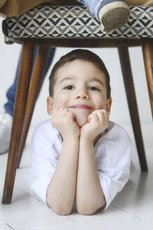 Lächelnder Junge, der sich mit den Ellbogen unter einen Stuhl stützt - EYAF02674