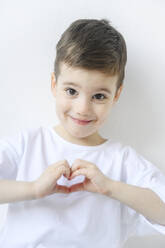 Lächelnder Junge mit Herzgeste vor weißem Hintergrund - EYAF02683