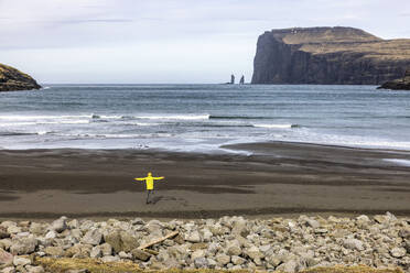 Mann schaut auf die Meeresstacke Risin und Kellingin am Strand stehend - WPEF07354