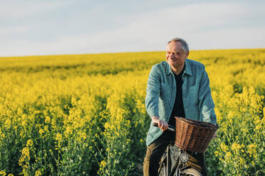 Smiling senior man riding bicycle in rapeseed field - VSNF00836