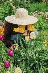 Frau mit Hut riecht an Tulpen im Garten - VSNF00858