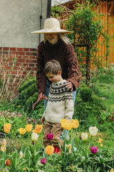 Mutter und Sohn stehen neben Tulpen im Garten - VSNF00859