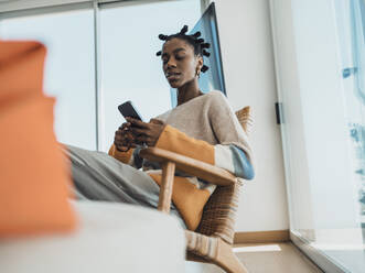 Young woman using smartphone sitting in armchair at home - MFF09327