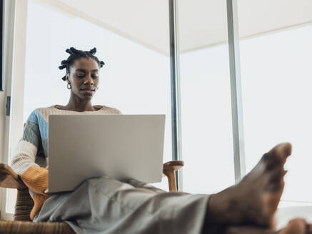 Man sieht eine junge Frau, die bequem in einem Sessel zu Hause sitzt und ihren Laptop zum Arbeiten oder zum Surfen im Internet benutzt - MFF09333
