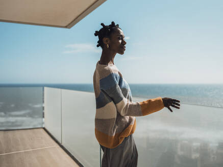 Woman in casual clothes standing at glass railing on balcony - MFF09346