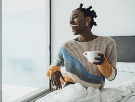 Eine fröhliche Frau genießt ihren Morgenkaffee, während sie sich zu Hause im Bett entspannt - MFF09360