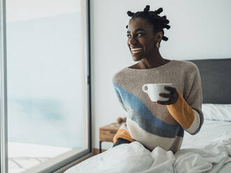 Eine zufriedene Dame, die ihren Morgenkaffee genießt, während sie gemütlich auf dem Bett sitzt - MFF09361