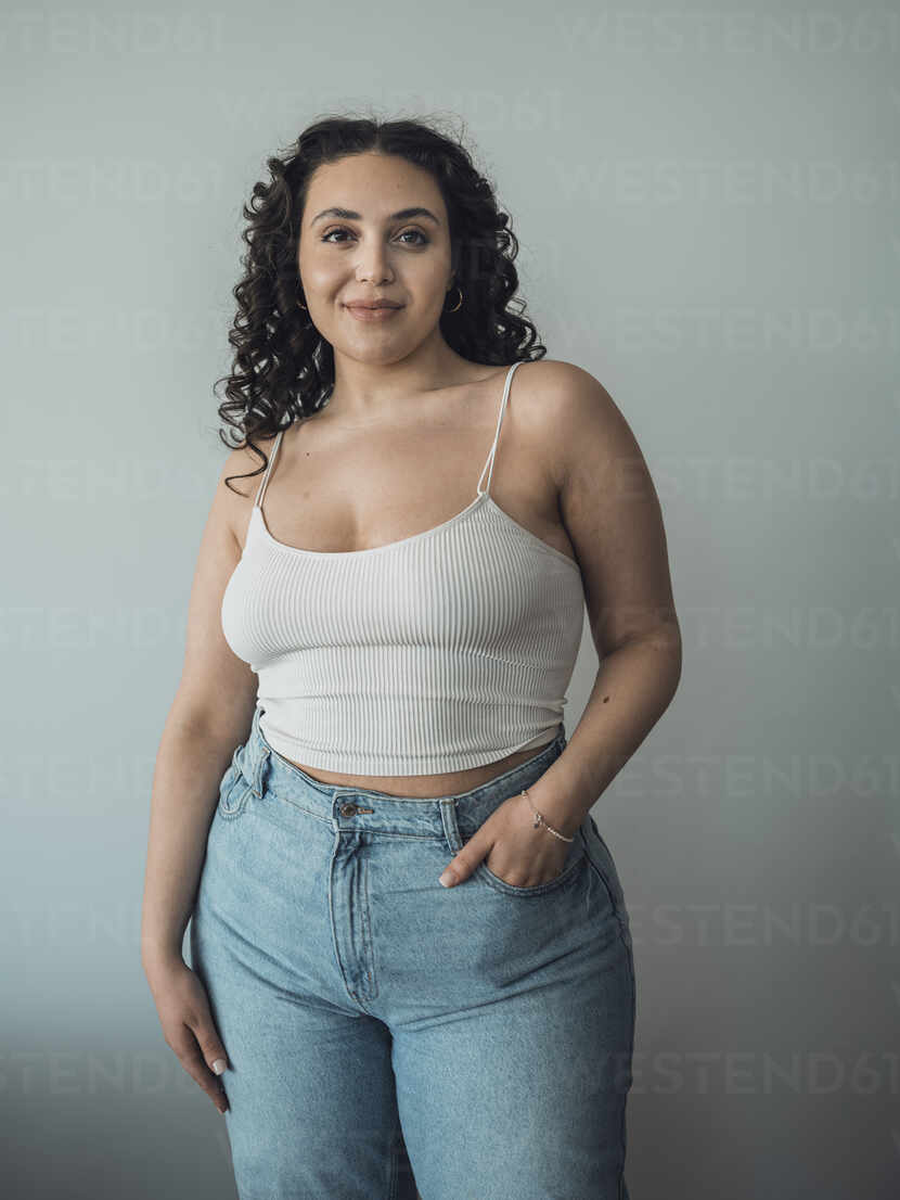 Curvy woman with hand in pocket standing in front of wall stock photo