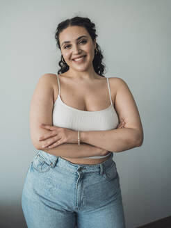 Smiling young woman standing with arms crossed in front of wall - MFF09378