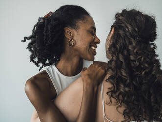 Zwei Freundinnen teilen einen glücklichen Moment, während die eine liebevoll ihre Hand auf die Schulter der anderen legt - MFF09387