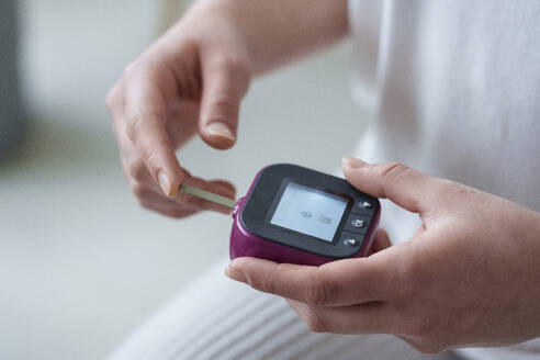 Hands of woman using digital glucometer at home - AAZF00491