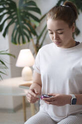 Woman using digital glucometer sitting at home - AAZF00492