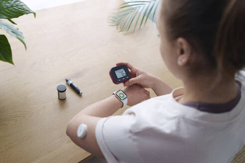 Woman with diabetes synchronizing smart watch and glucometer at home - AAZF00505