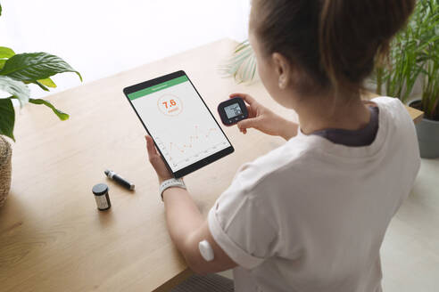 Woman with diabetes synchronizing tablet computer and glucometer at home - AAZF00507