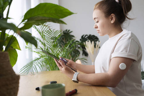 Woman with diabetes synchronizing tablet PC and glucometer on table at home - AAZF00508