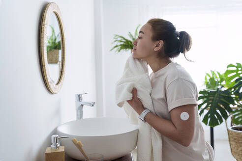 Woman with diabetes cleaning face with towel in bathroom at home - AAZF00513