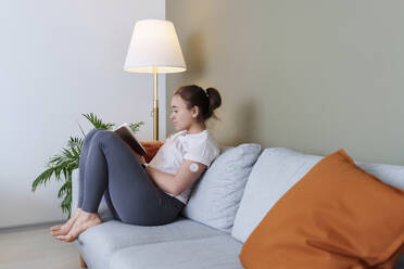 Frau mit Diabetes liest ein Buch auf der Couch zu Hause - AAZF00529