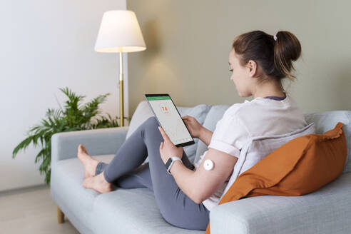Frau mit Diabetes, die zu Hause auf der Couch sitzt und einen Tablet-PC benutzt - AAZF00531