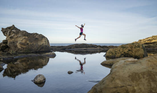 Woman jumping over rocks near sea - SNF01630