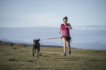 Smiling woman running with dog on grass - SNF01634
