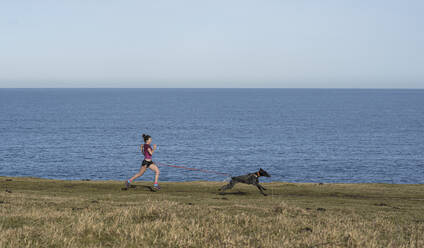 Young woman running with dog near sea - SNF01637