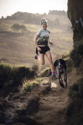 Happy woman running with dog on dirt road - SNF01645