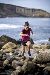 Happy woman running over rocks in sea - SNF01646