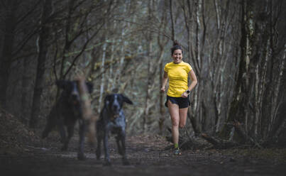 Happy woman running on footpath with dogs in forest - SNF01649