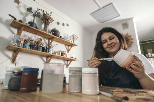 Smiling potter painting ceramic pot at workshop - ADF00044