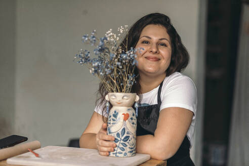 Smiling potter with ceramic flower vase at workshop - ADF00053