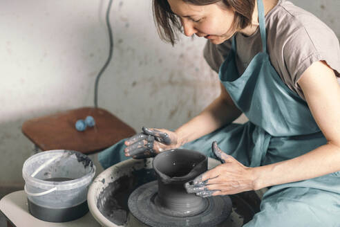 Töpfer mit Schürze bei der Herstellung eines Keramiktopfes in einer Werkstatt - ADF00058