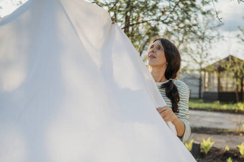 Frau trocknet weißes Bettlaken auf der Wäscheleine im Hinterhof - ANAF01422