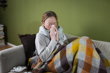 Sick young woman sneezing in tissue relaxing on couch - MIKF00349