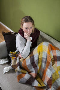 Kranke junge Frau, eingewickelt in eine Decke, entspannt auf der Couch - MIKF00351