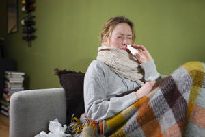 Kranke junge Frau benutzt Nasenspray und entspannt sich auf der Couch - MIKF00353