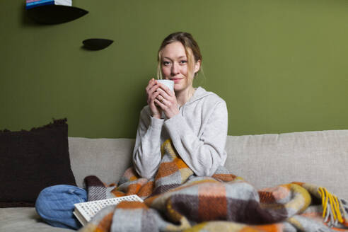 Junge Frau mit Tasse auf der Couch liegend - MIKF00354