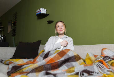 Thoughtful young woman with book relaxing on couch - MIKF00359