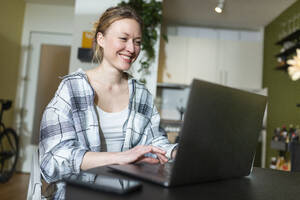 Lächelnde Geschäftsfrau, die zu Hause mit einem Laptop arbeitet - MIKF00368