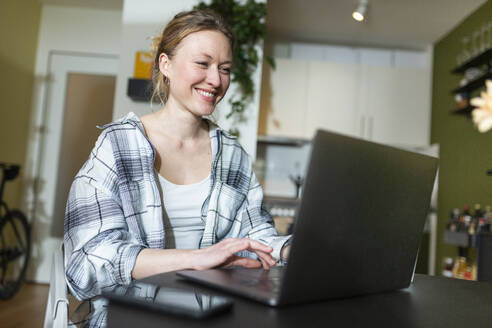 Smiling businesswoman working with laptop at home - MIKF00368