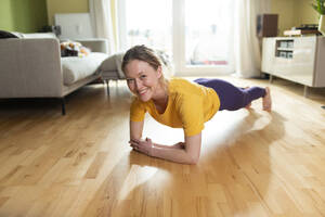 Smiling young woman doing plank position at home - MIKF00380